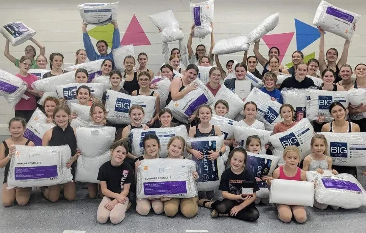 A large group of girls holding up donated pillows they collected