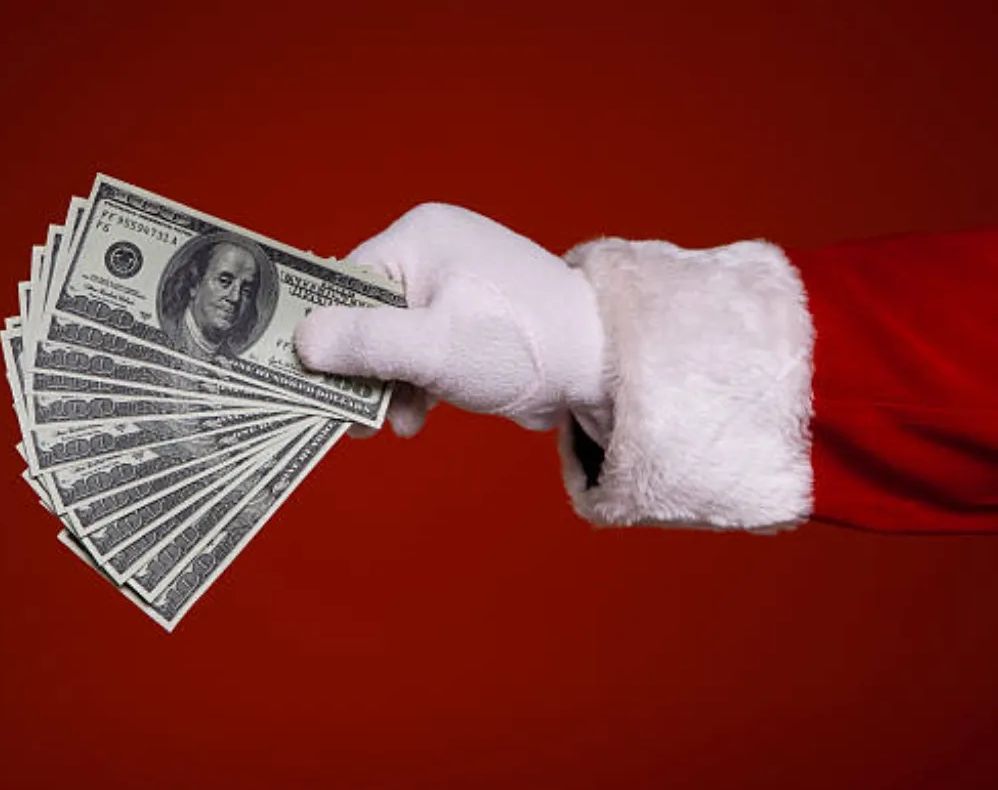 Santa's gloved hand holding a fan of dollar bills