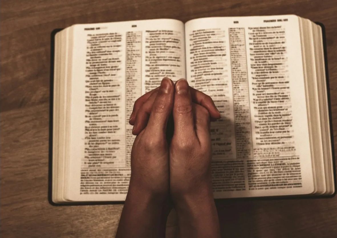 Hands folded in prayer over an open Bible
